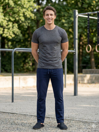 Men's dark grey t-shirt and navy blue sweatpants, standing with hands behind back.