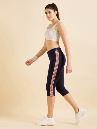 Women in a standing pose wearing navy blue capri leggings with a pink stripe print and a white crop top.