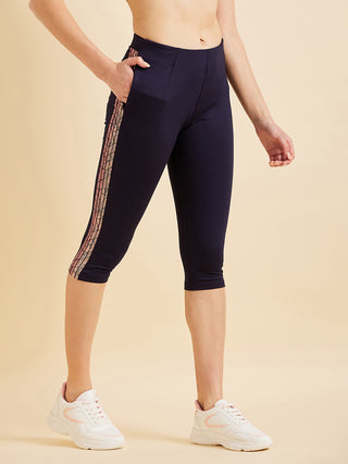 Women posing wearing navy blue capri leggings with a decorative stripe and white sneakers, a slight variation from the previous image.