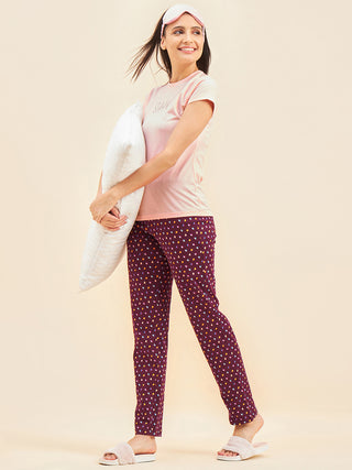 Women in a pink t-shirt with "SHHH... I'M GOING BACK TO BED" printed on it and burgundy printed pajama pants stand holding a pillow.