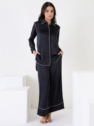 A woman in black piped pajamas sits on the floor.