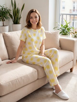 A woman in lemon-print pajamas sits on a beige sofa.