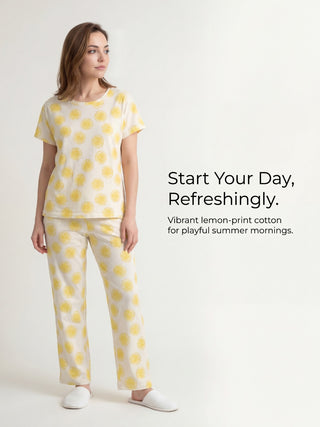 A woman in a cream-colored pajama set with a yellow lemon print, standing with her body facing left and looking to the side.