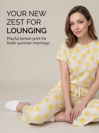 A woman in lemon-print pajamas sits on a beige sofa.