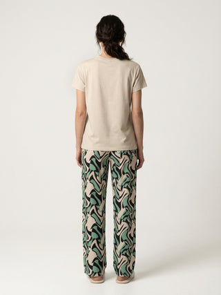 A woman stands facing away from the camera, wearing a cream t-shirt and patterned pajama pants.