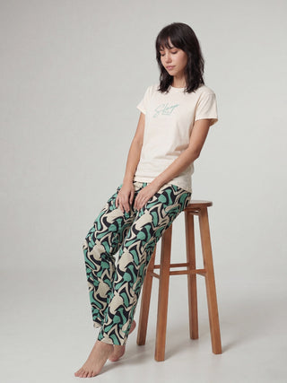 A woman stands facing away from the camera, wearing a cream t-shirt and patterned pajama pants.
