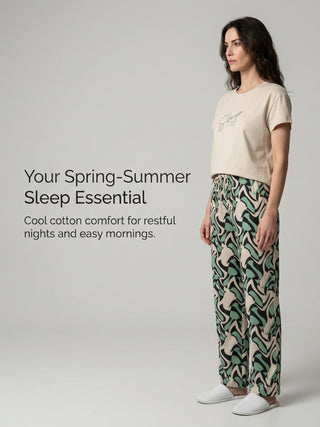 A woman poses in a cream-colored t-shirt with "Sleep" printed on it, and green and black patterned pajama pants.