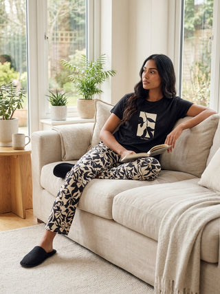 A woman sits on a couch wearing black pajamas with a floral print.