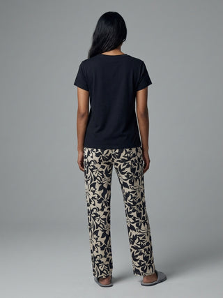 Women's black short-sleeved t-shirt and beige pants with a black floral print, posing from behind.