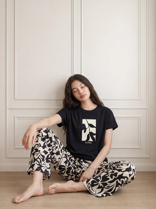 Women's black short-sleeved t-shirt and beige pants with a black floral print, posing from behind.
