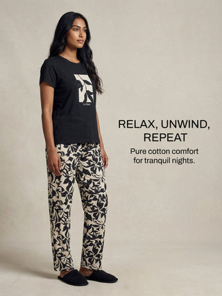 A woman in a black pajama set with a floral print, posing on a plain background.