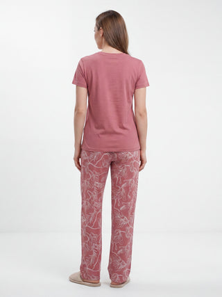 Woman in pink floral pajama set with slippers, viewed from the back.