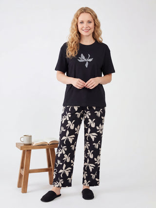 A woman standing and wearing a black t-shirt with a floral print and black floral print pants.