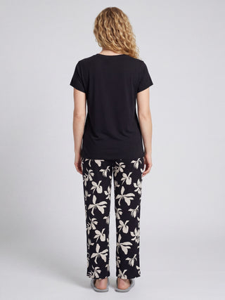 Woman in navy blue pyjama set with white floral print, standing and looking away from the camera.