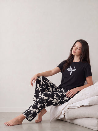 Woman in navy blue pyjama set with white floral print, standing and looking away from the camera.