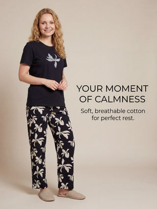 Woman in navy blue pyjama set with white floral print, standing and looking towards the camera.