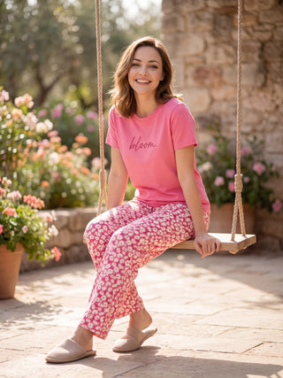 Woman in pink t-shirt with "bloom" graphic and pink floral print pajama pants, sitting on a swing.