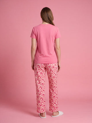 A woman models a pink short-sleeved t-shirt and floral-print pajama pants, standing with her back to the camera.