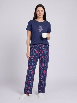A woman in a navy blue t-shirt with a palm tree graphic and matching patterned pajama pants with pink and blue wavy lines.