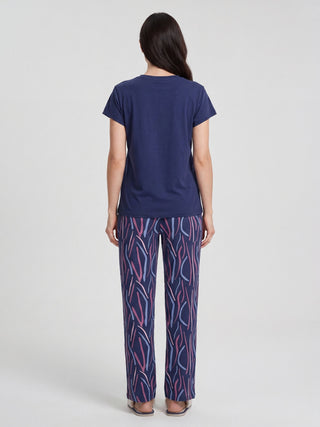 Women, standing from behind wearing a navy blue t-shirt and patterned pajama pants with blue, pink, and purple lines.