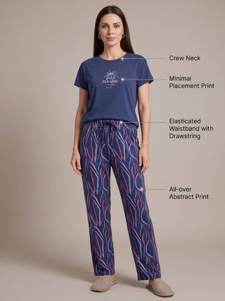 A woman in a navy blue pajama set with an all-over abstract print and a "Palm Paradise" graphic on the top, standing and posing.