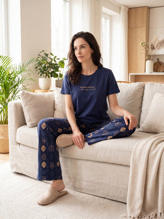 Woman in navy blue pajama set with geometric print, sitting on a couch.