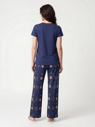 A woman stands with her back to the camera, wearing a navy blue t-shirt and navy blue patterned pajama pants.