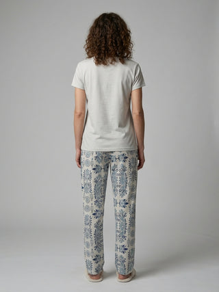 Women's light grey t-shirt and cream pajama pants with a blue paisley print, standing from the back.