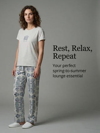A woman models a light-colored pajama set with blue and white patterned pants and a matching top, posing to the left.