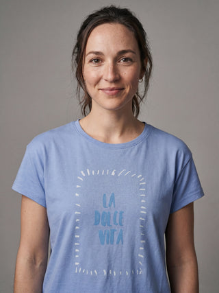 A woman wearing a light blue t-shirt with "LA DOLCE VITA" printed on it, posing for a portrait.