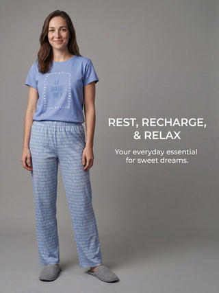 A woman wearing a light blue t-shirt with "LA DOLCE VITA" printed on it and blue patterned pajama pants, standing and posing for a portrait.