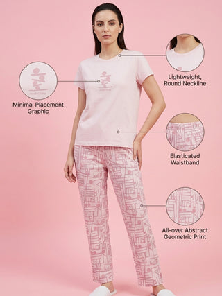 A woman stands wearing pink pajama pants with a geometric print and a pink t-shirt featuring a minimal placement graphic.
