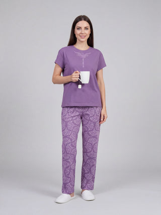 A woman poses in a purple pajama set with a white mug and a white teabag.