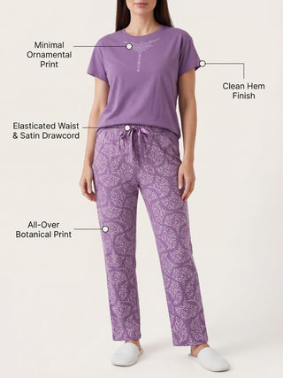 Women wearing a purple pajama set with an ornamental print on the top and a botanical print on the pants, standing against a white background.