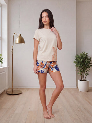 A woman in beige pajamas with a botanical print and elasticated waistband sits on the floor.
