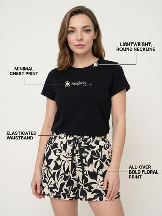 A woman wearing a black t-shirt with a "Simplicity" logo and floral print shorts is featured in a full-body studio shot.