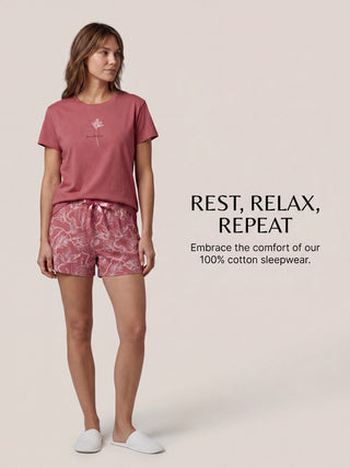 A woman models a rose-colored sleepwear set with a floral print, embracing comfort.