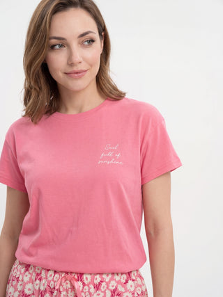 A woman poses wearing a pink t-shirt with "Soul full of sunshine" text print and floral pajama bottoms.