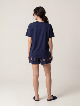 Women wearing navy blue t-shirt and shorts with abstract print, standing with back to camera, wearing slippers.