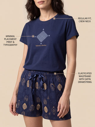 A woman is shown modeling a navy blue pajama set with a unique geometric print, featuring a crew neck top and drawstring shorts.
