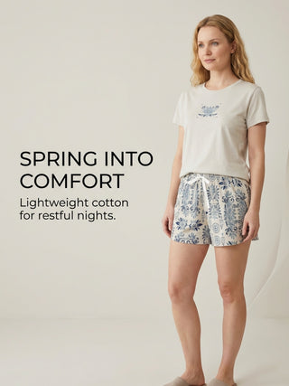 Woman wearing a light grey t-shirt with a blue floral print and matching light grey shorts with a blue paisley print.