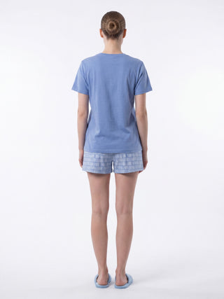 Women wearing a blue t-shirt and patterned blue shorts, standing from the back.