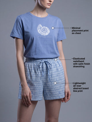 Women, posing from the front, wearing light blue short-sleeved t-shirt with a white ammonite print and light blue shorts with a white abstract print.