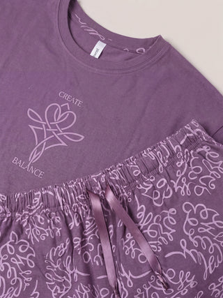 Women's purple pajama set with "CREATE BALANCE" graphic print and a swirling pattern.