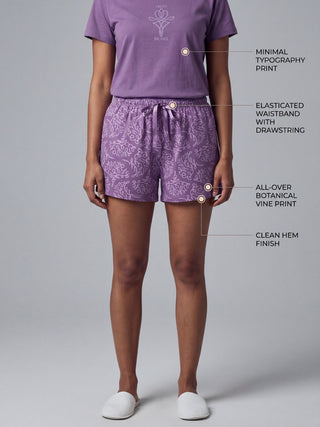 Women in a standing pose wear purple pajama shorts with an all-over botanical vine print and a matching t-shirt with a minimal typography print.