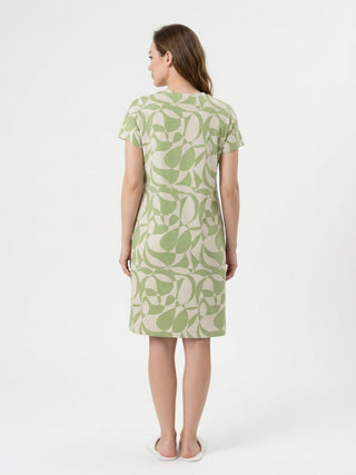 Women, wearing a short-sleeved, green and beige patterned shift dress, stands facing away from the camera.