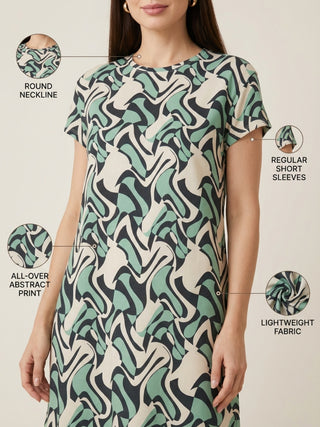 A woman wears a flowing dress with a multicolored abstract print, featuring a round neckline and short sleeves.