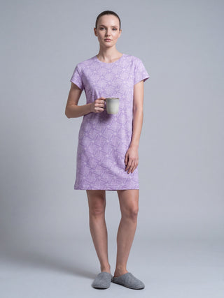 Woman in a lavender floral print short-sleeve sleep dress standing and holding a mug, wearing grey slippers.