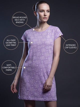 A woman in a lilac all-over geometric leaf print sleep shirt with extended cap sleeves, a broad round neck with binding, and soft, comfortable fabric.