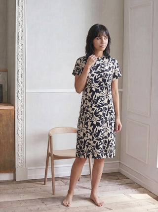 Women in a relaxed pose wearing a beige and black floral print lightweight dress with a round neckline.